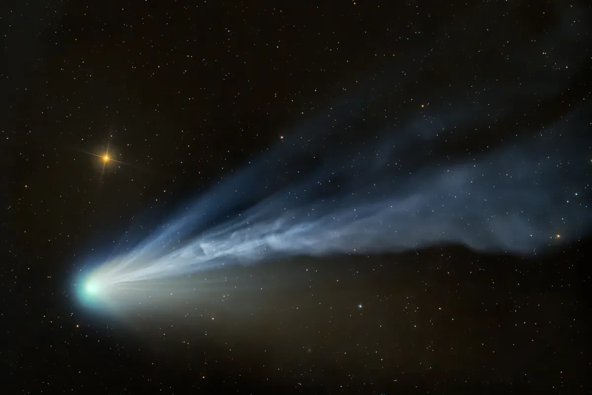 A bright blue comet with a long cloud-like tail in a black, starry sky.